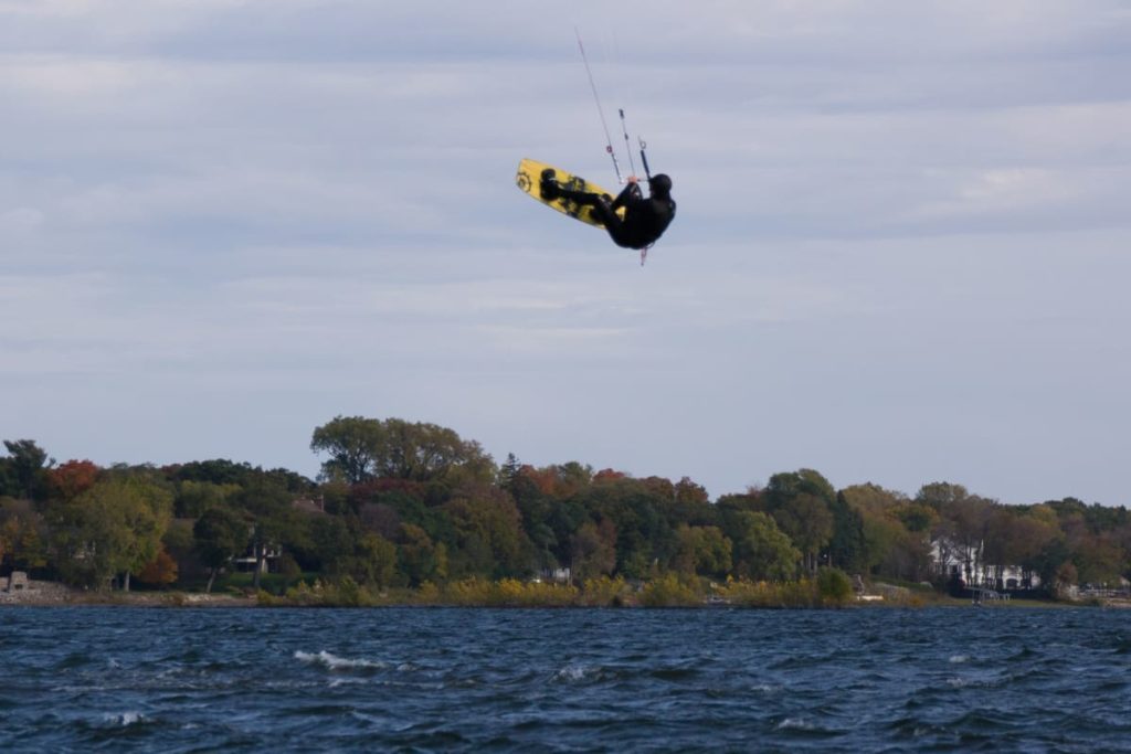 Kiteboarder performing a very high jump off the water while wearing a wetsuit