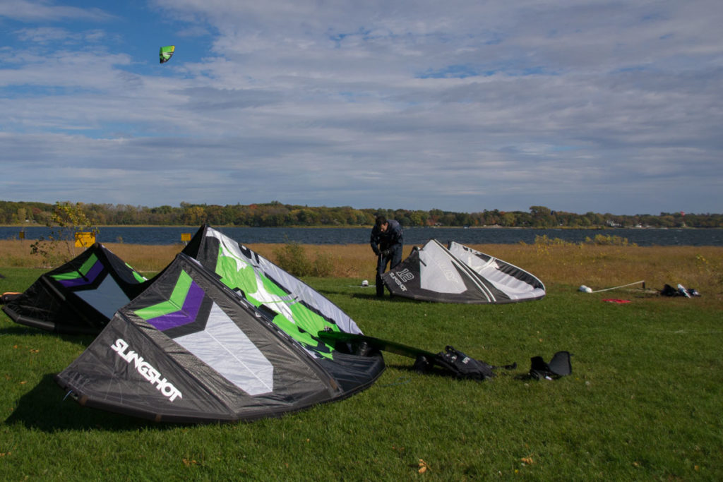 A kiteboarder is rigging a kite up on the shore of White Bear Lake