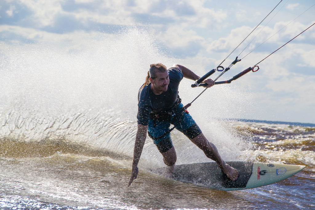 A kitesurfer slashes a wave with a large smile on his face.